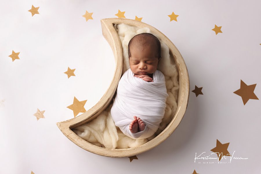 Indian baby boy sleeping wrapped in white in a moon prop against a star background during his photoshoot