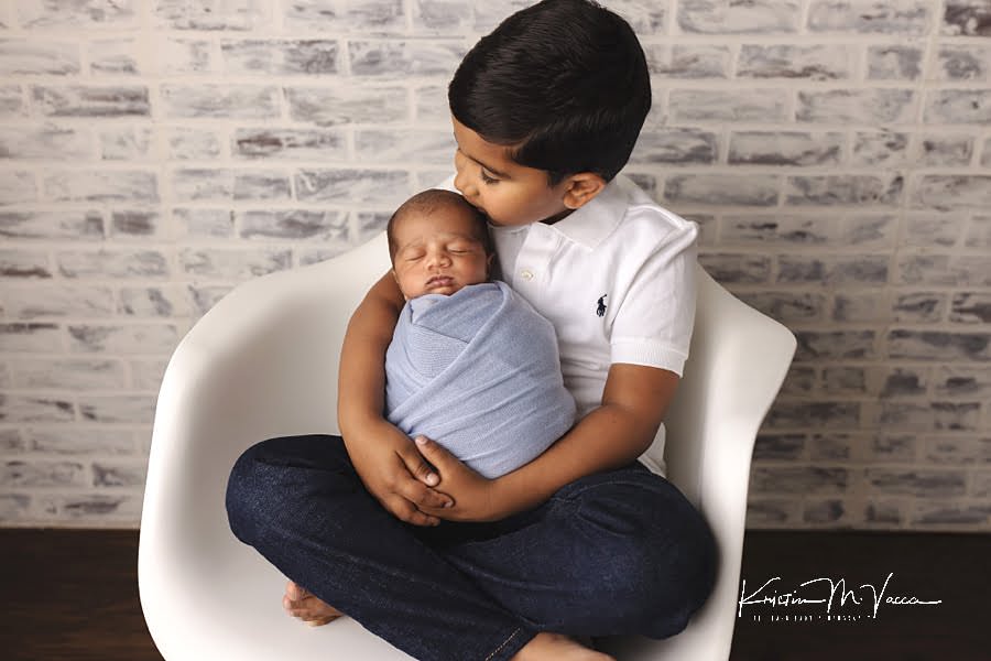 Indian big brother kisses his sleeping newborn baby brother on the head during their photoshoot