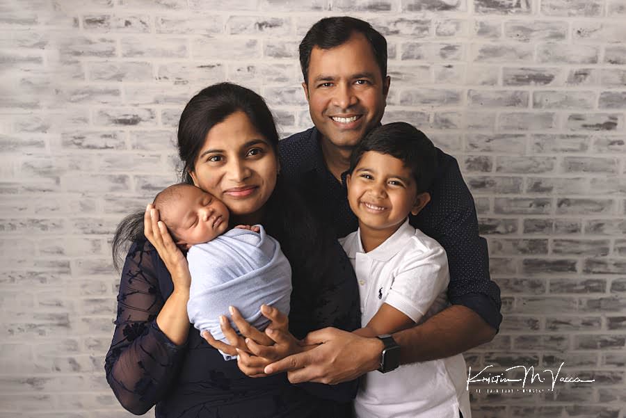 Smiling group photo of an Indian family posing during their newborn photos with older brother