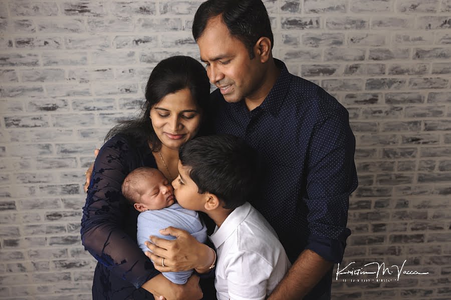 Indian family looking down as big brother kisses baby brother on the head during their photoshoot