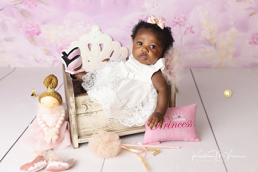 Black baby girl sitting in a white cradle with her pink heels during her princess baby photos by The Flash Lady