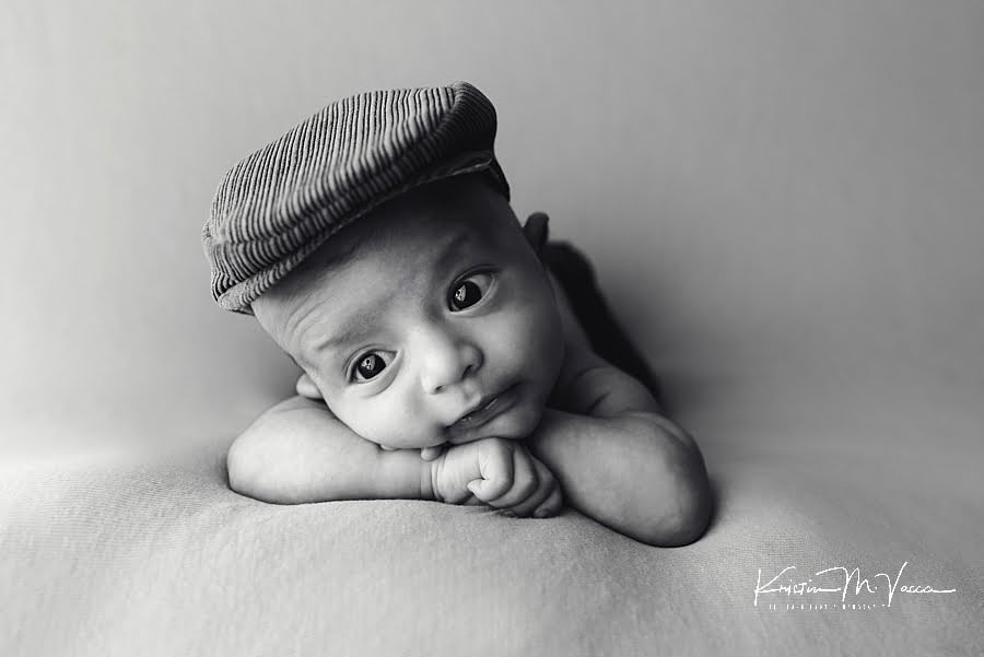 Black and white photo of a wide awake newborn boy in a newsboy hat during his photoshoot