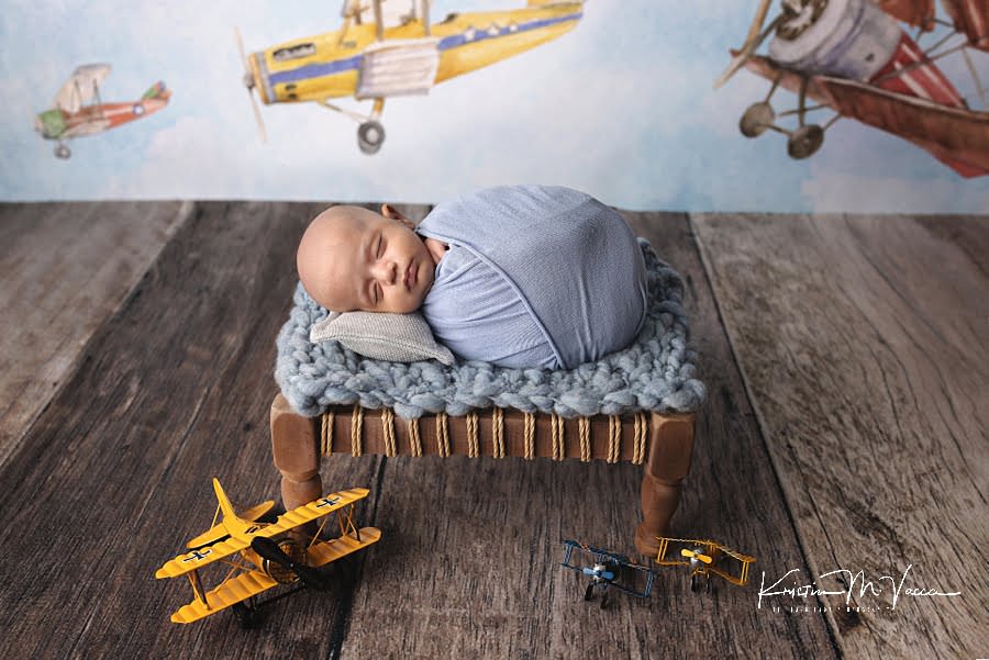 Baby boy sleeping on a blue blanket amongst tin airplanes during his photoshoot
