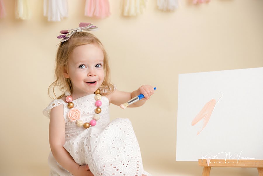 Surprised toddler girl holding a paint brush ready to paint during her photoshoot