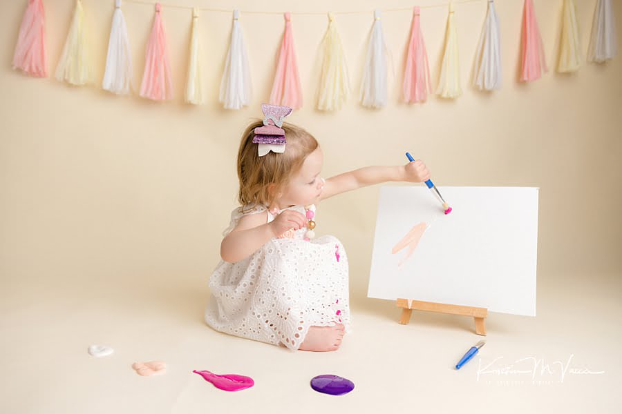 Toddler girl painting a canvas with pink paint during her photoshoot