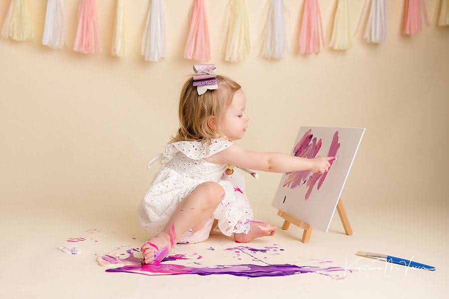 Toddler girl painting a canvas with her finger during her photoshoot