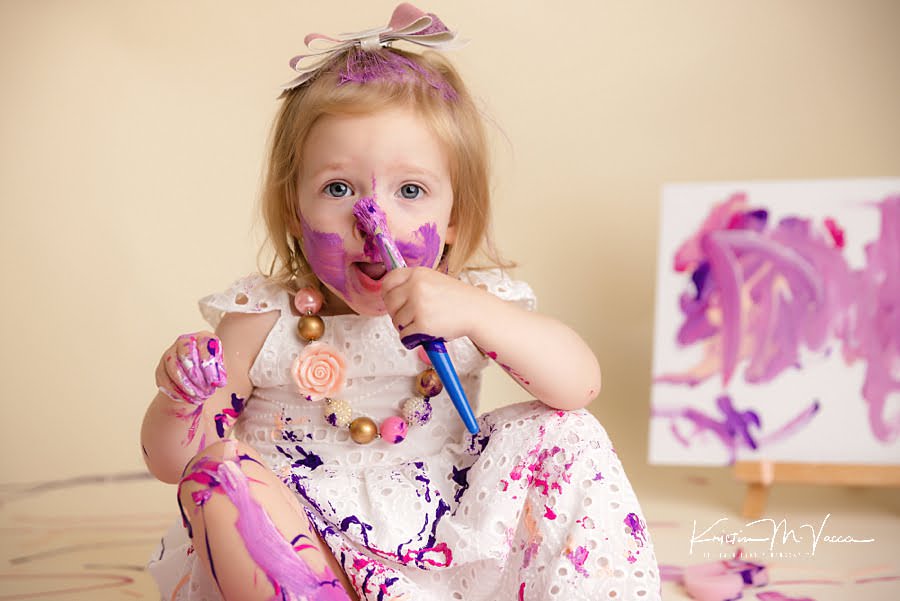 Toddler girl painting her nose purple and pink during her photoshoot