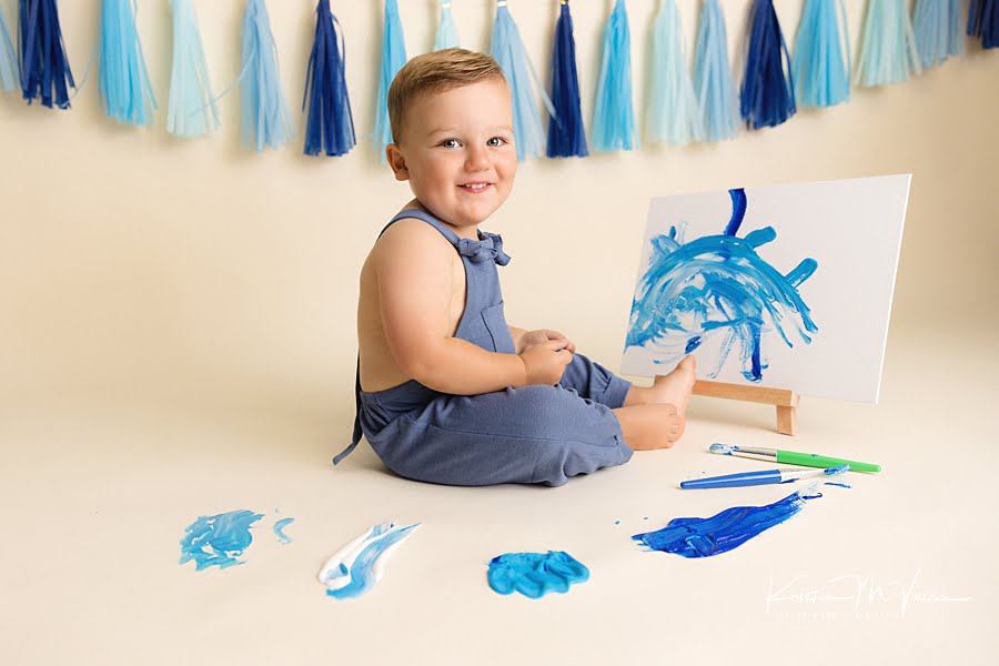Smiling toddler boy proud of his painted canvas during his birthday photoshoot