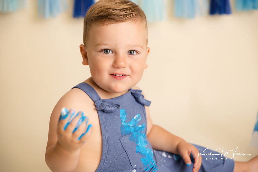 Close up of a smiling toddler boy with paint on his hands and overalls during his photoshoot