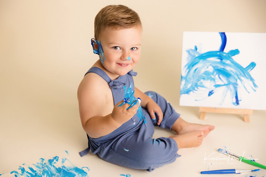 Sly smile from this toddler boy as he paints his face during his blue paint smash