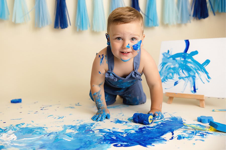 Smiling toddler boy preparing to roll paint on the floor during his blue paint smash
