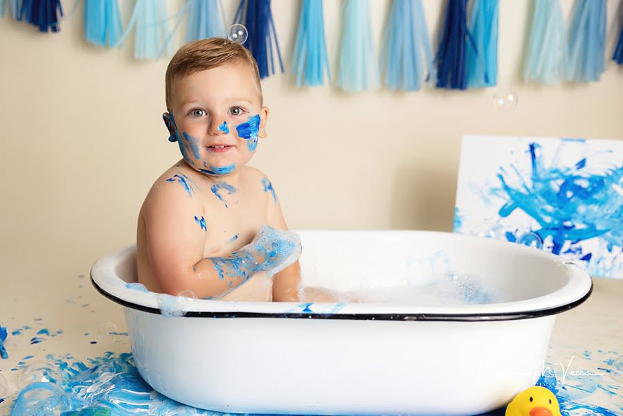 Toddler boy sitting in a bathtub after his blue paint smash