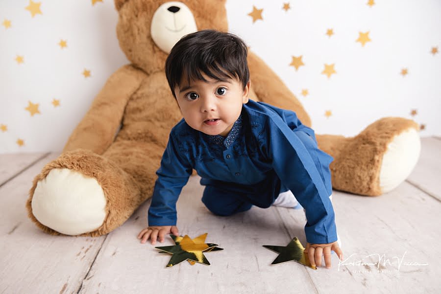 Toddler boy crawling towards gold stars during his first birthday photoshoot