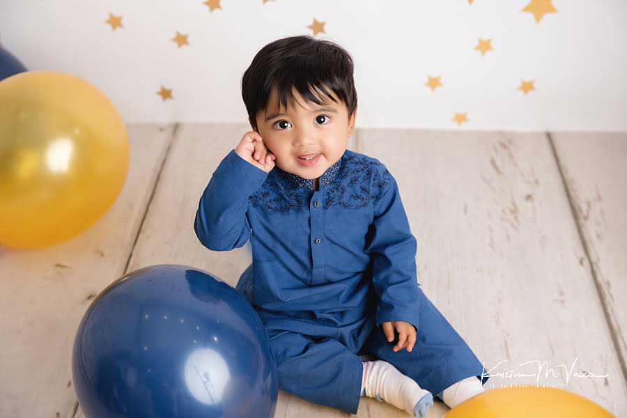 Toddler boy smiling surrounded by balloons during his birthday photoshoot