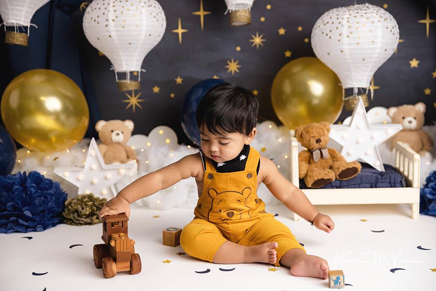 Toddler boy pushing a toy during his blue and gold teddy cake smash