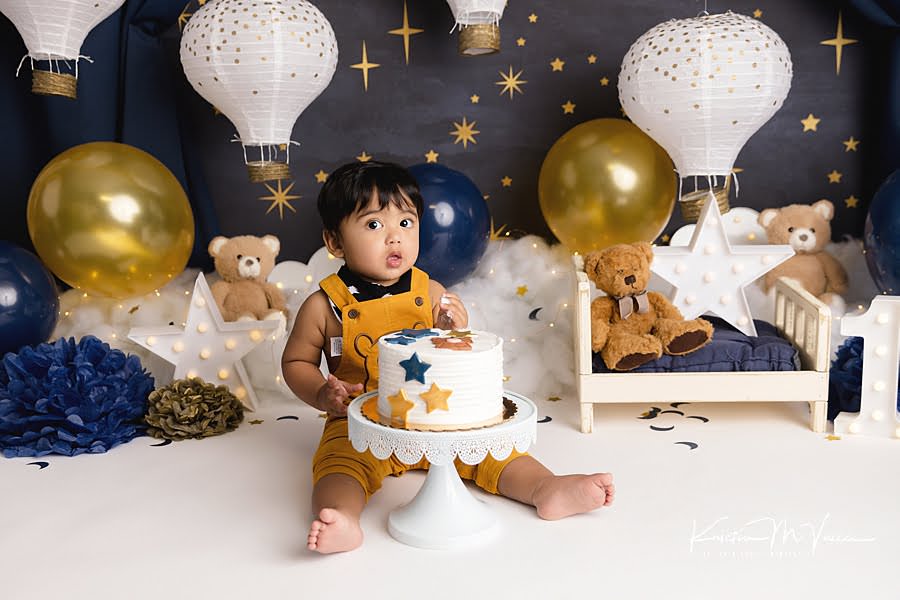 Toddler boy prepares to dive into his cake during his blue & gold teddy cake smash