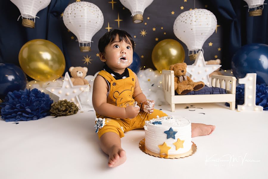 Toddler boy looks up at his parents during his blue & gold teddy cake smash