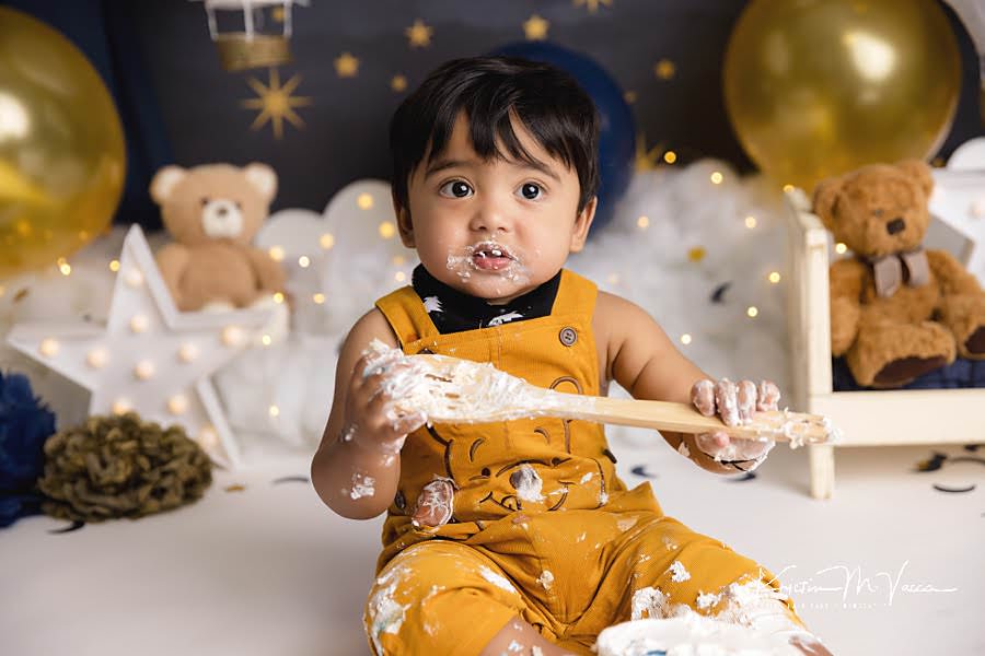 Toddler boy hold onto a wooden spoon during his birthday cake smash