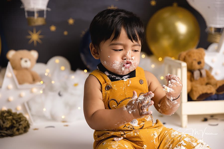 Toddler boy makes a silly face while looking at his hands during his cake smash