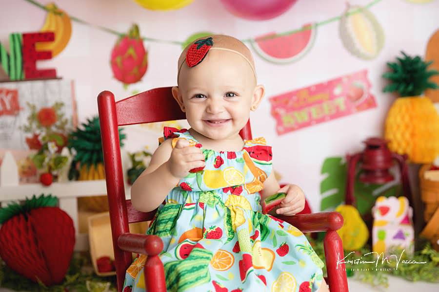 Smiling toddler girl in a fruit patterned dress during her fruit cake smash