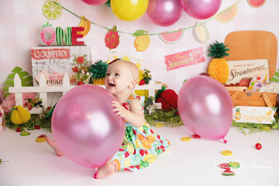 Baby girl laughing while holding a pink balloon during her fruit cake smash