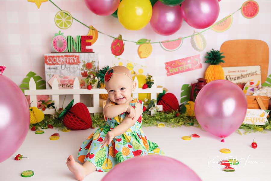 Smiling baby girl batting a pink balloon during her birthday photoshoot