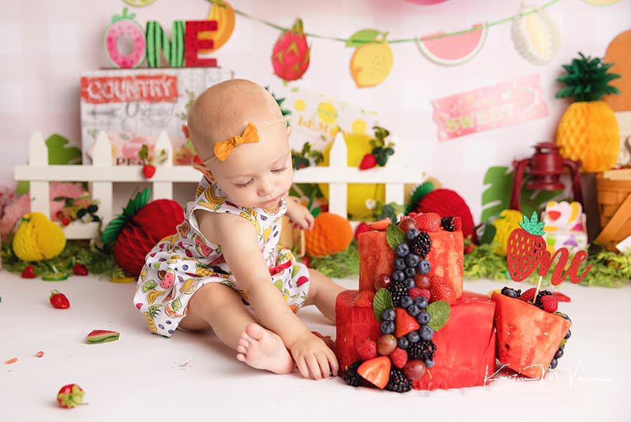 Toddler girl reaches for fruit pieces from her watermelon cake during her photoshoot