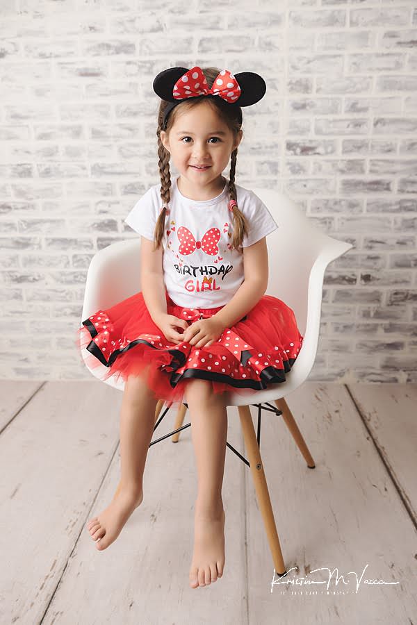 Young girl sits in a red and white dress during a birthday photoshoot