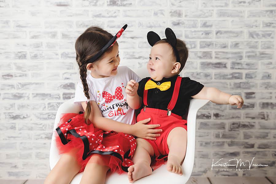 Sister and brother smile at each other during their mickey carnival cake smash photoshoot