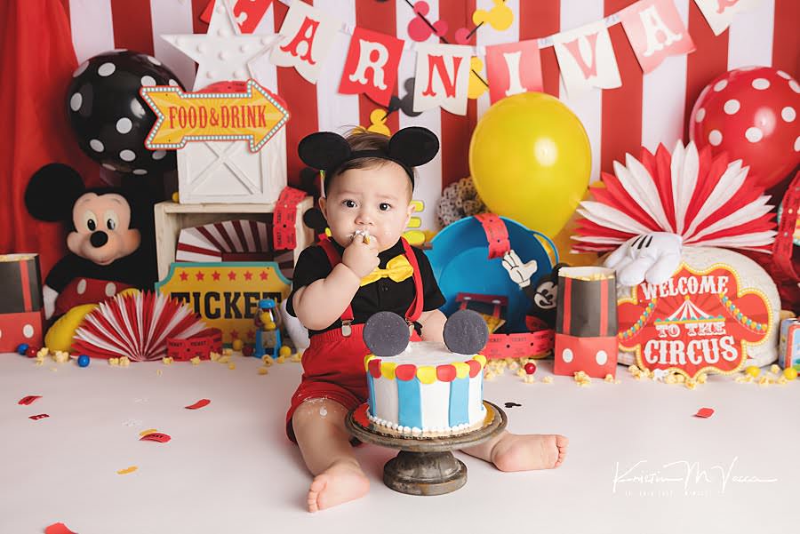 Toddler boy stars eating his cake during his mickey carnival cake smash photoshoot