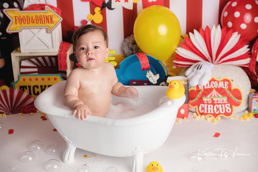 Toddler boy looks at the camera while sitting in a bath tub during his birthday photoshoot