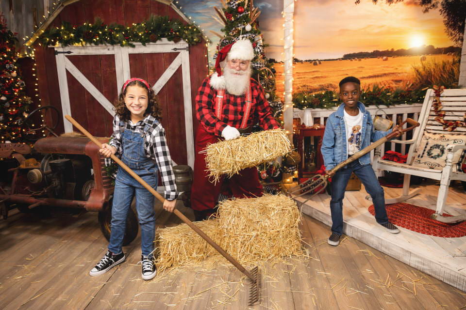 Santa Claus poses with a young boy and girl raking hay during their Christmas photoshoot