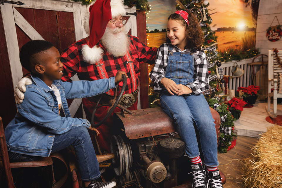 Young girl and boy sitting on a tractor during their farmhouse Christmas photos with Santa