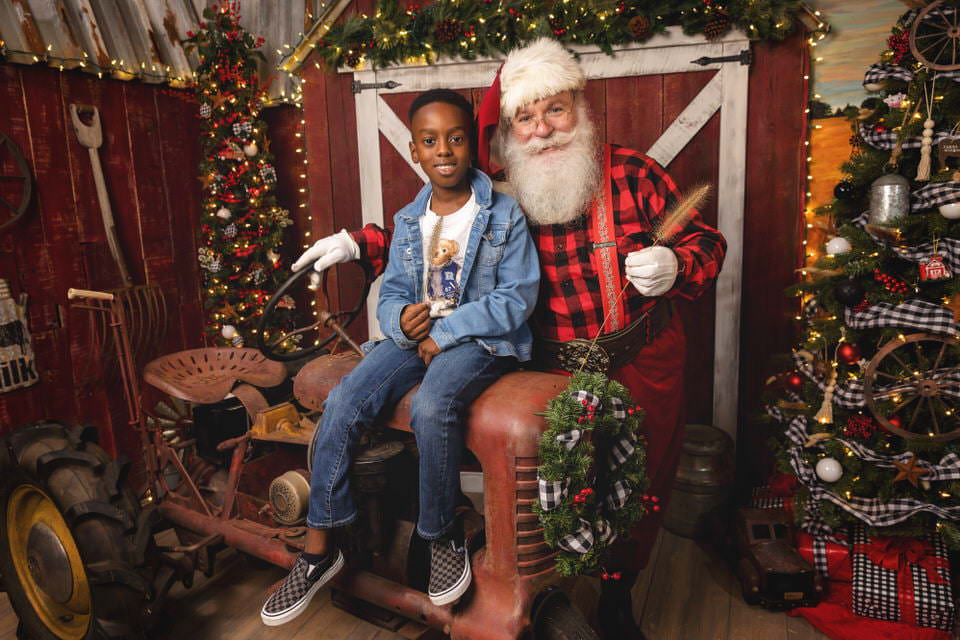 A young black boy sits with Santa Claus on an antique tractor during his Christmas photoshoot