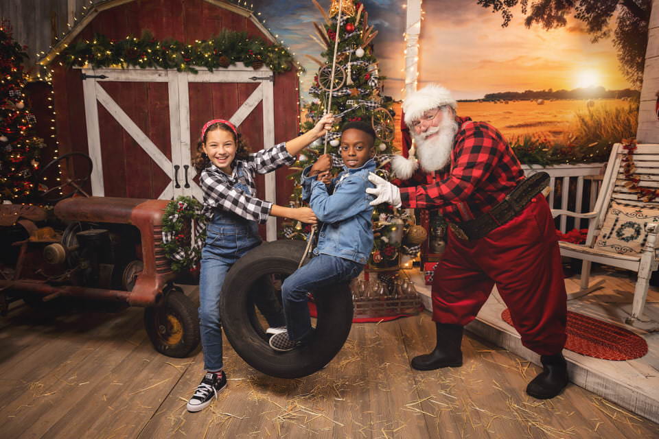 Young girl and Santa Claus pushing a boy on a tire swing at The Flash Lady Photography's Farmhouse Christmas