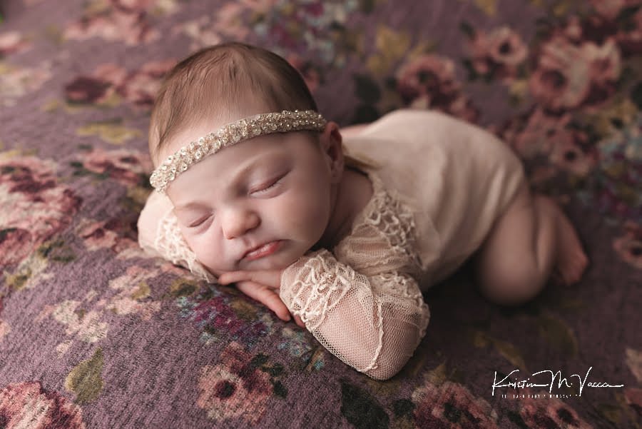Sleeping baby girl on a purple floral blanket posing on her hands during her summer newborn photos