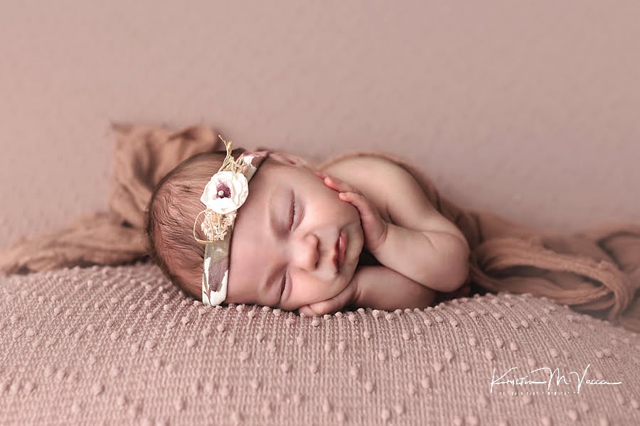 Sleeping baby girl on a mauve blanket with her hands under her chin during her newborn photoshoot