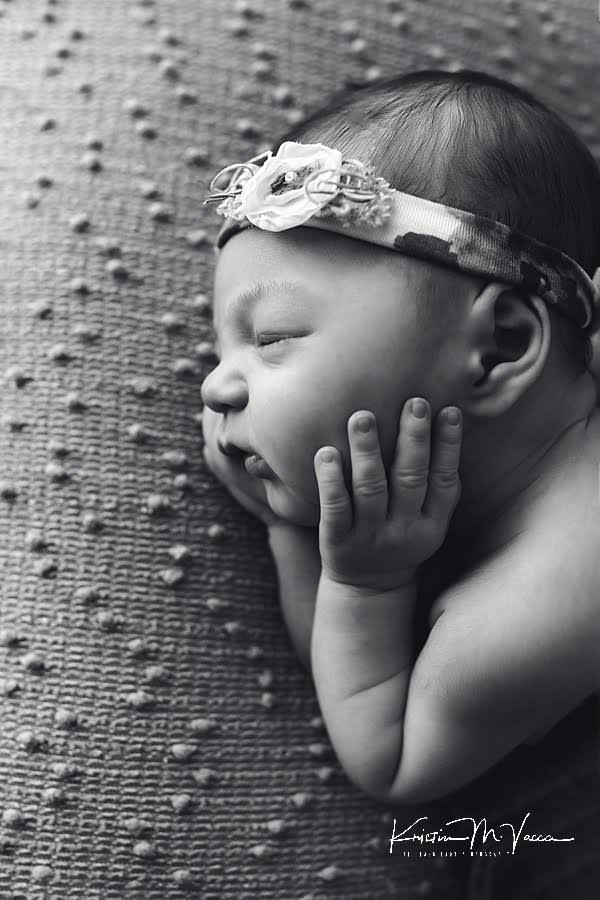 Black and white photo of a sleeping newborn baby girl with her hands on her cheeks during her photoshoot