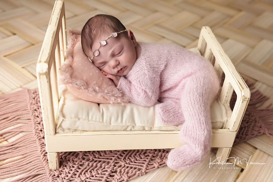 Newborn baby girl sleeping on a cream bed with pink pjs during her photoshoot