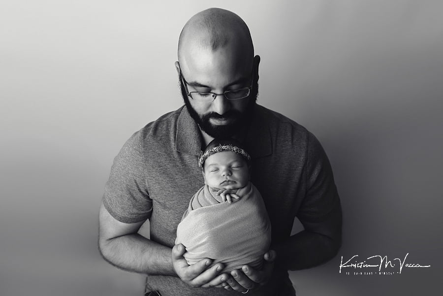 Black and white photo of a Dad holding his newborn baby in his hands during their photoshoot