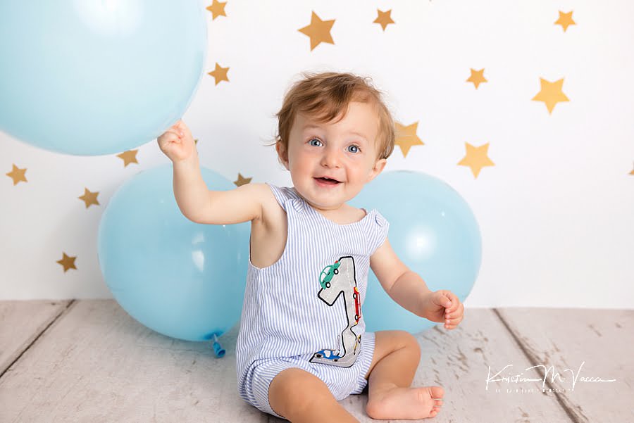 Toddler boy smiling while playing with a balloon during his first birthday photoshoot