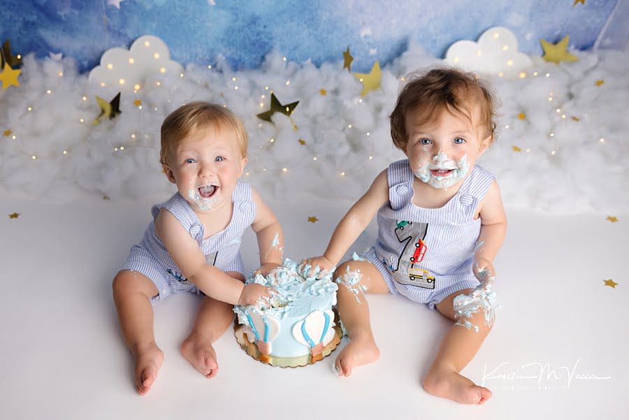 2 smiling toddler boys looking up at the camera during their twin balloon cake smash