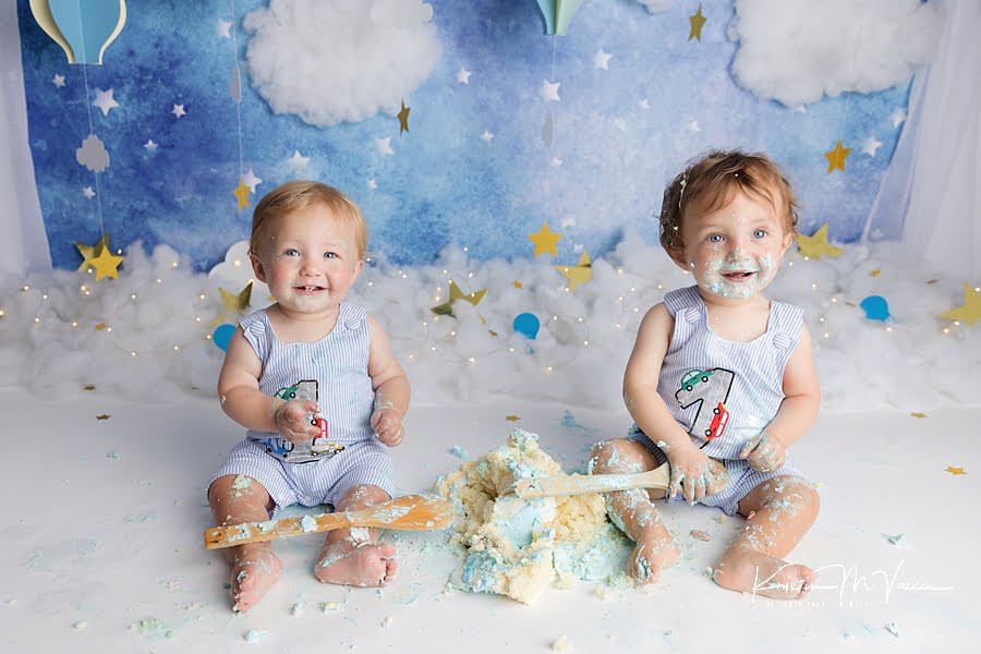 2 smiling boys covered in frosting during their twin balloon cake smash