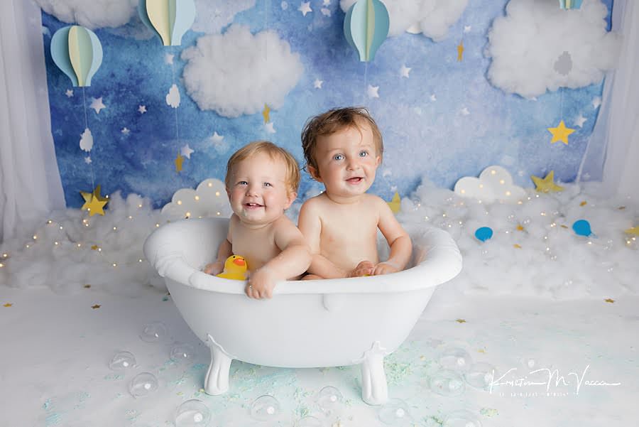 2 smiling toddler boys taking a bath in a tub during their twin balloon cake smash