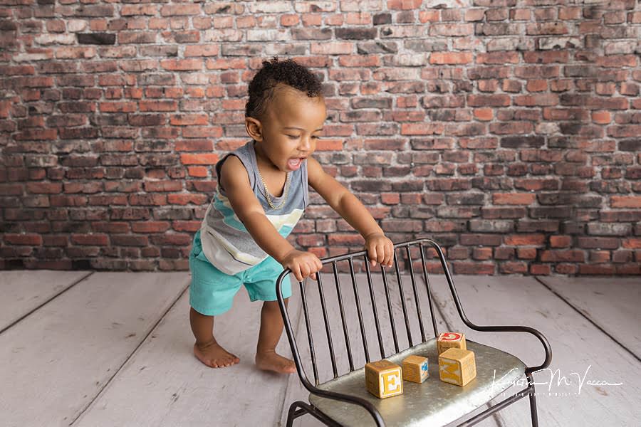 Toddler boy playfully pushes a bench with blocks during his birthday photoshoot