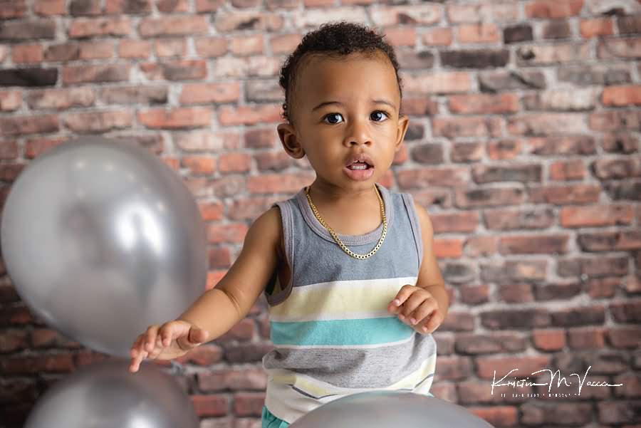 Toddler boy looks at balloons during his birthday photoshoot