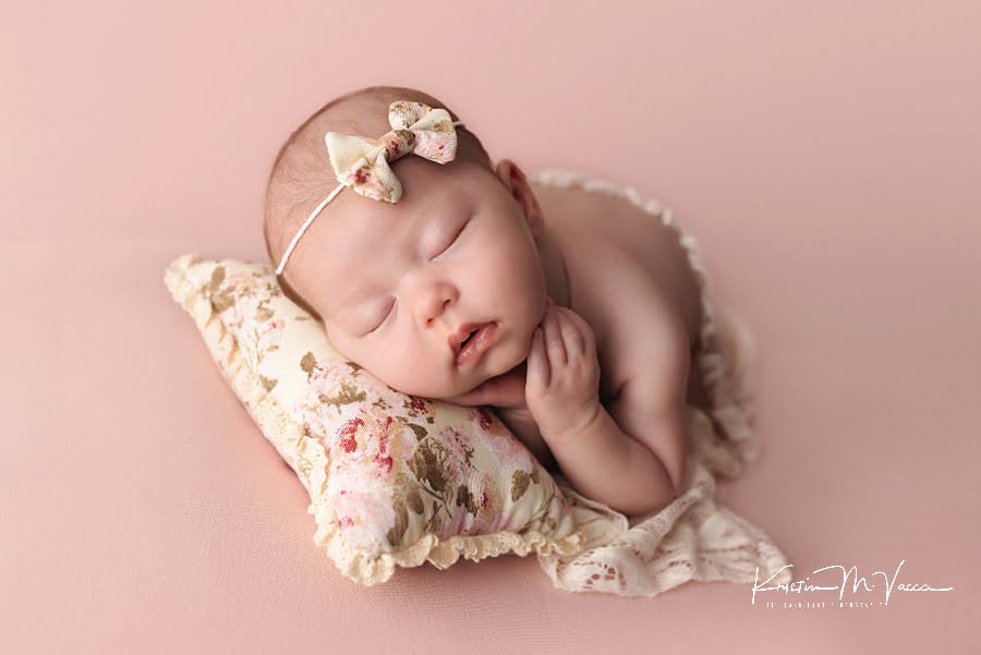 Sleeping baby girl holds her cheeks on a floral pillow during her photoshoot
