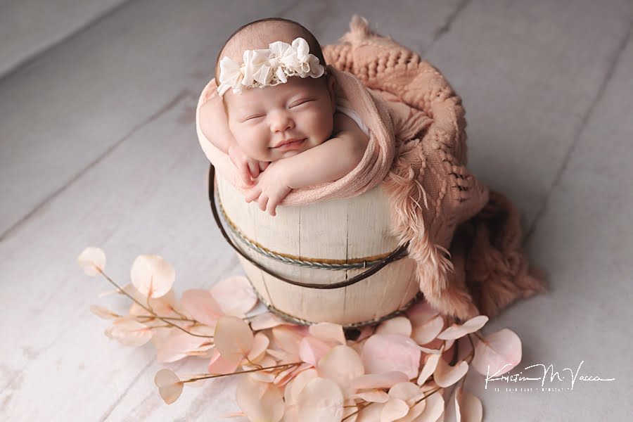 Sleeping newborn baby girl smiles in a bucket during her photoshoot