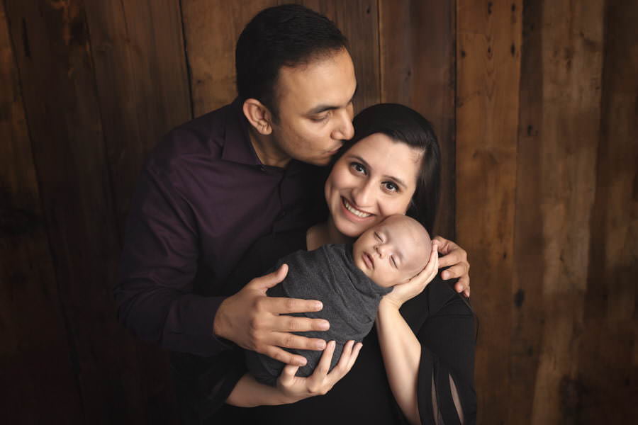 Indian Dad kisses the Mom holding their newborn baby boy during their photoshoot