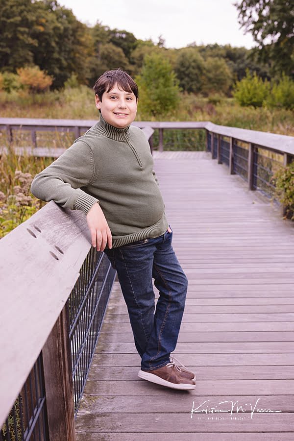 Teen boy leans against a boardwalk railing during their early fall family photos